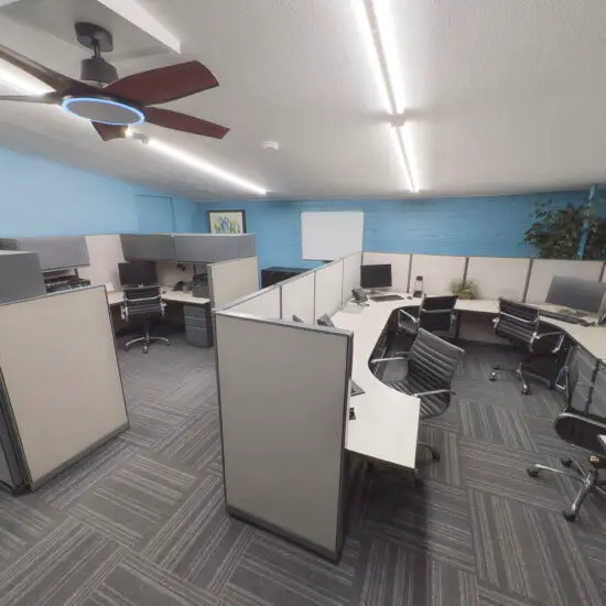 Modern office space with grey and white cubicles, black chairs, and blue walls